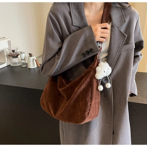 Detail of brown suede Hobo bag featuring a white fluffy cloud pendant and wide strap