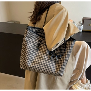 Detail of large houndstooth tote bag with black leather straps and elephant charm