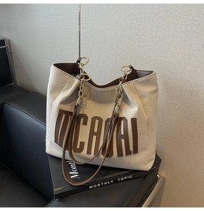 Detail of canvas tote bag with brown leather trim and metal chain strap on magazines