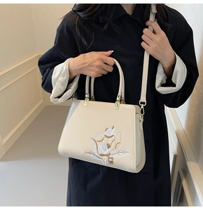 Detail of floral embroidery on cream leather tote bag with elegant gold-tone hardware