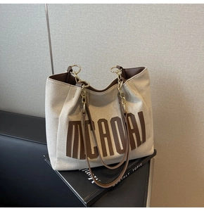 Detail of beige canvas tote bag with brown leather MEADAJ lettering and gold metal rings