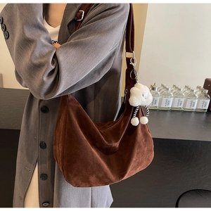 Detail of dark brown faux suede crescent tote bag with a plush cloud charm on a model
