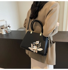 Detail of elegant black handbag with intricate white tulip floral embroidery and handles
