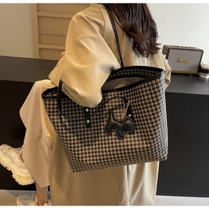 Detail of large houndstooth tote bag with black strap and cute puppy pendant on a model