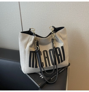 Detail of grey woven tote bag featuring black leather trim and gold chain handle