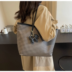 Detail of houndstooth tote bag with black leather straps and a puppy charm pendant