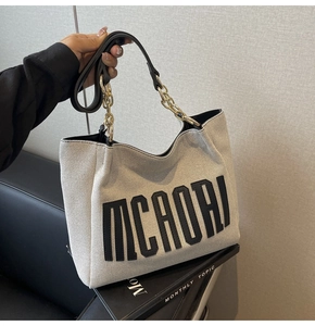 Detail of canvas tote bag featuring MCAORI leather patch and metal chain strap