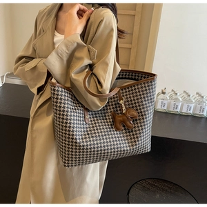 Detail of large houndstooth tote bag with brown leather straps and puppy charm
