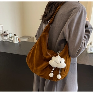 Brown faux suede hobo bag with adjustable strap and white cloud pendant in cafe setting