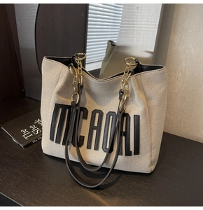 Detail of canvas tote bag featuring metallic chain strap and black letter embroidery