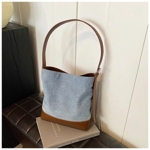 Detail view of denim bucket bag featuring brown leather trim and metallic buckles