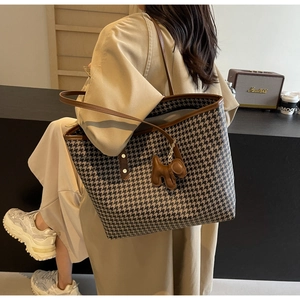 Detail of large houndstooth tote bag with brown straps and cute dog charm on a model