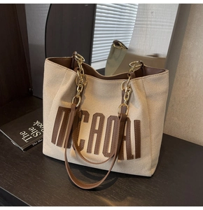 Close-up of canvas tote bag featuring brown leather MICAOAI patch and chain strap