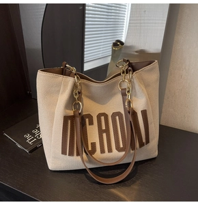 Detailed macro view of high-quality canvas tote bag with brown leather trim and metal chains