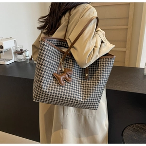 Detail of houndstooth tote bag with brown leather trim and cute dog charm decoration