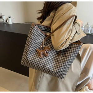 Detail of houndstooth tote bag with brown leather trim and a cute puppy charm