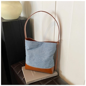 Detail of blue denim and brown leather bucket bag shown in a lifestyle interior setting