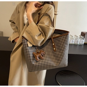 Detail of houndstooth tote bag with brown leather trim and cute puppy charm on model