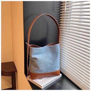 Detail of blue denim bucket bag with brown leather bottom on a white book surface