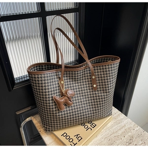 Close-up of houndstooth tote bag with brown leather trim and a cute puppy bag charm