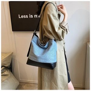 Close-up of light blue denim and black leather bucket bag worn with khaki trench coat