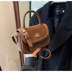 Detail of a brown leather and suede handbag showing golden oval twist lock and stitching