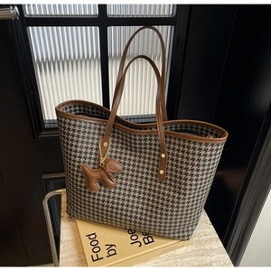 Detail of houndstooth tote bag featuring brown leather trim and a cute puppy charm
