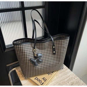 Close-up of houndstooth tote bag texture with black leather trim and decorative charm