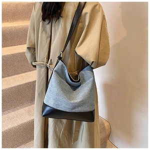 Detail of blue denim bucket bag with black leather base worn on shoulder with a trench coat