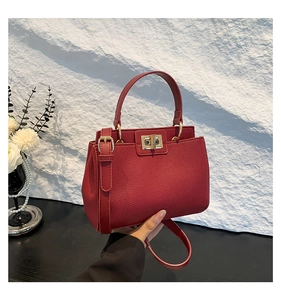 Close-up of red lychee pattern leather handbag with gold swivel lock and shoulder strap