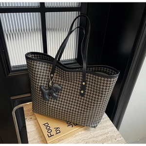 Macro shot of houndstooth tote bag with a black leather dog charm and gold chain detail