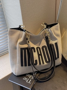 Chic beige canvas tote bag with black letter print and leather strap in natural lighting