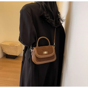 Detail of retro brown leather handbag showing mixed textures and metal oval swivel lock