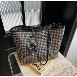 Detail of houndstooth tote bag featuring a leather dog charm and sleek shoulder strap