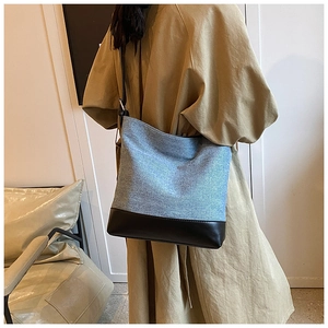 Detail view of denim fabric and black leather stitching on a large bucket shoulder bag