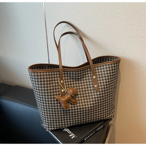 Close-up of houndstooth tote bag with brown leather handles and a puppy-shaped charm