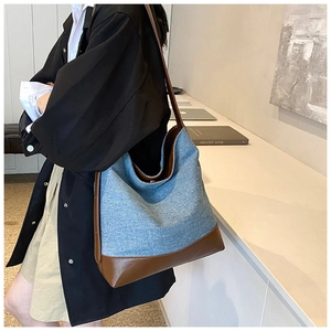 Detail view of denim bucket bag with brown leather trim worn by model in minimalist setting