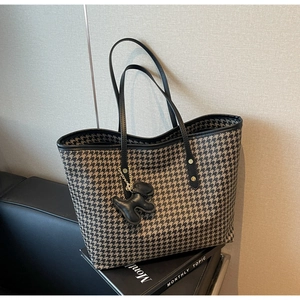 Detail of houndstooth tote bag featuring black leather handles and dog-shaped charm