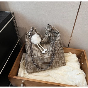 Detail of canvas tote bag with geometric stripes, chain strap and plush charm accent