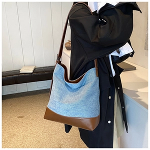 Detail of blue denim and brown leather bucket bag showing strap attachment and side profile