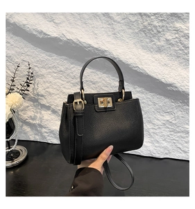 Detailed shot of a black pebbled leather handbag with a gold square clasp and round handle