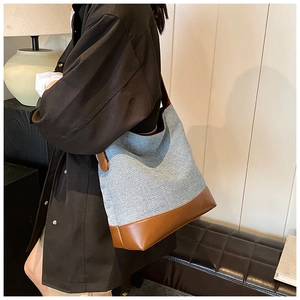 Detail shot of denim and brown leather bucket bag worn as a crossbody on a model