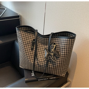 Detail of houndstooth tote bag with black leather trim and puppy charm on a book