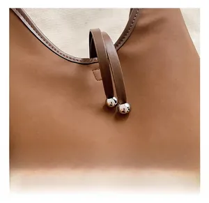 Detail of silver metal bead hardware on a brown PU leather shoulder bag with fine stitching