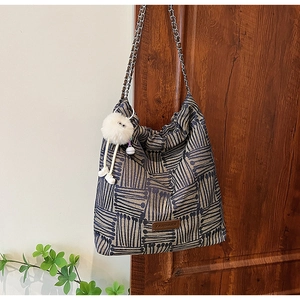 Detail of canvas bucket bag showing navy striped pattern and plush charm on a wooden door