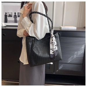 Detail of black embossed leather tote bag with woven handles and decorative silk scarf