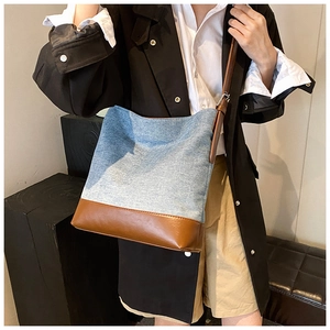 Detailed side view of a large denim bucket bag with brown leather trim worn cross-body