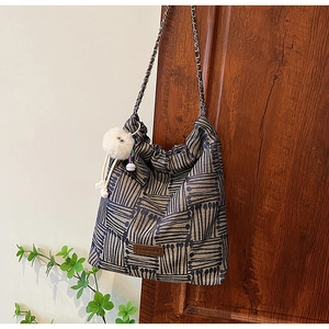 Detail view of woven striped tote bag with metal chain strap and plush ball charm