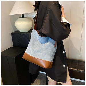 Detail of blue denim bucket bag with brown leather base shown on model in a modern room