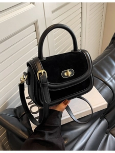Chic black composite leather handbag with gold hardware shown in a minimalist setting